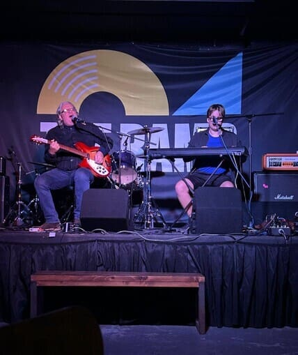 Two performers sat on a stage playing instruments