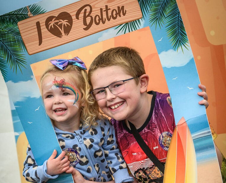 Two young children holding a selfie board smiling that says 'I love Bolton'