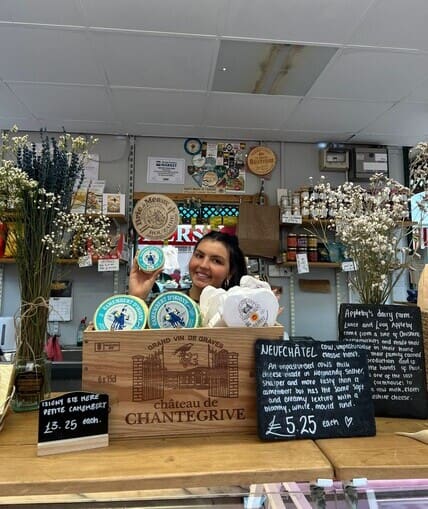 Young person standing behind a cheese counter promoting a variety of cheeses